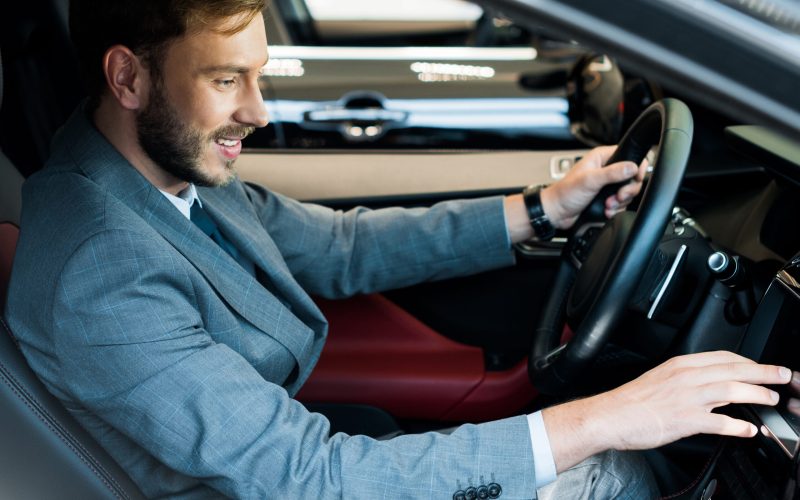 selective focus of cheerful bearded driver sitting on car and touching display selective focus of cheerful bearded driver sitting on car and touching display